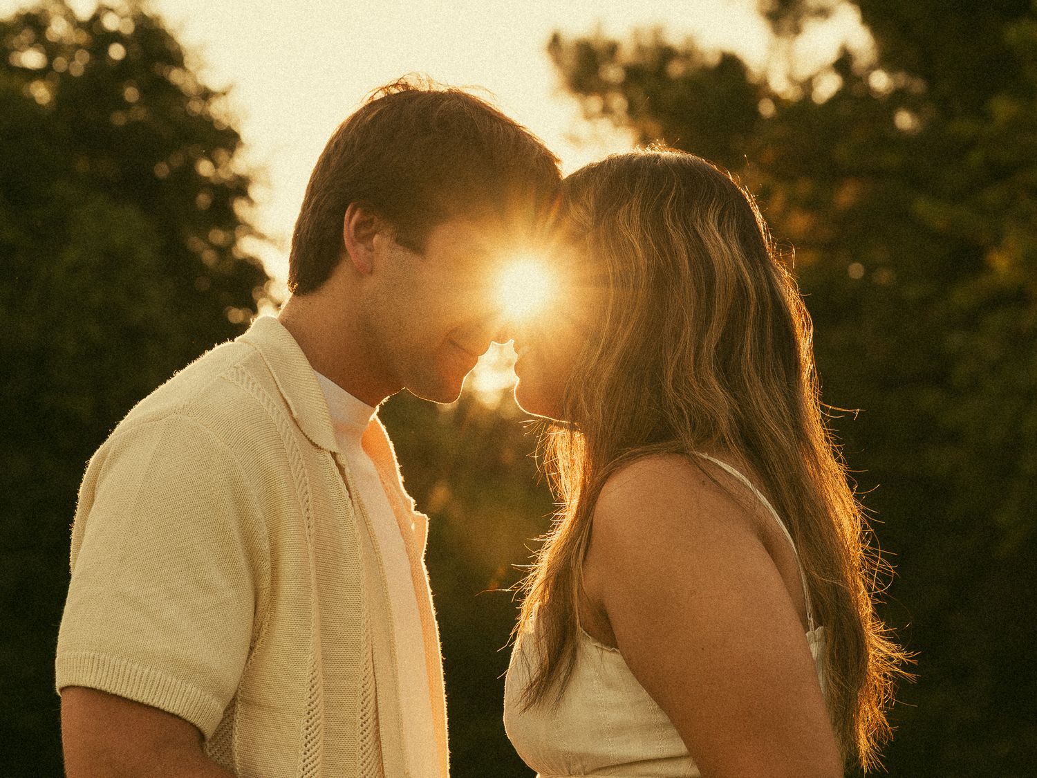 Romantic couple sharing an intimate moment at golden sunset with warm sunlight glowing between them outdoors.