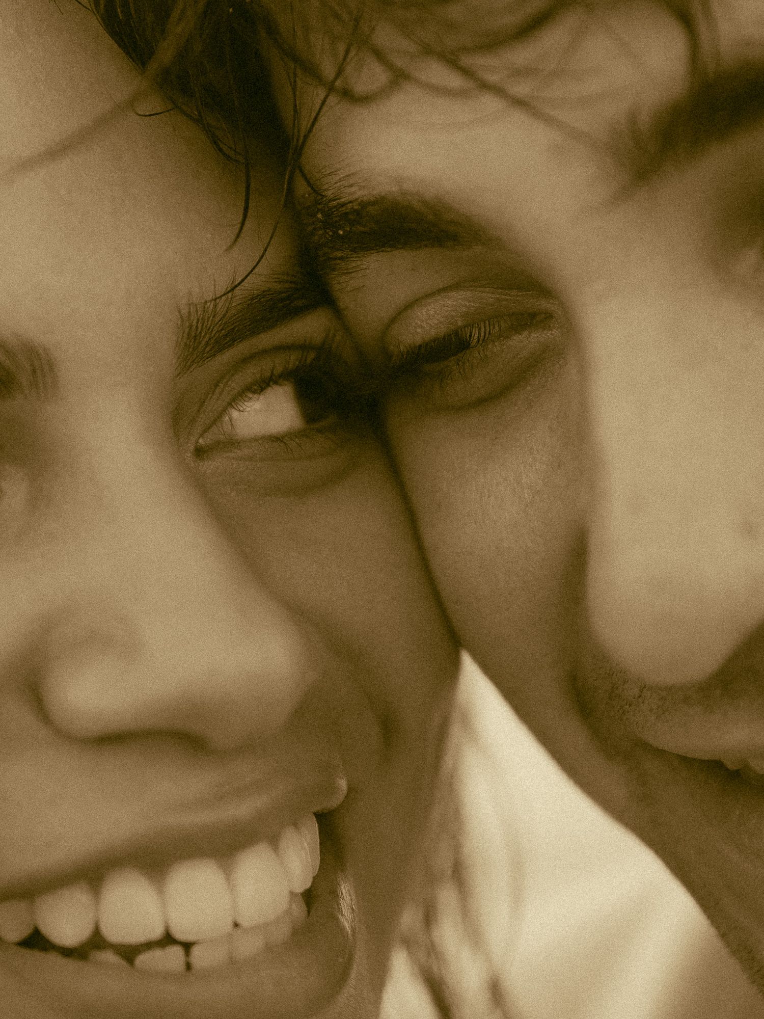 Close-up sepia portrait of two smiling people with dark curly hair cheek to cheek, radiating joy and connection.