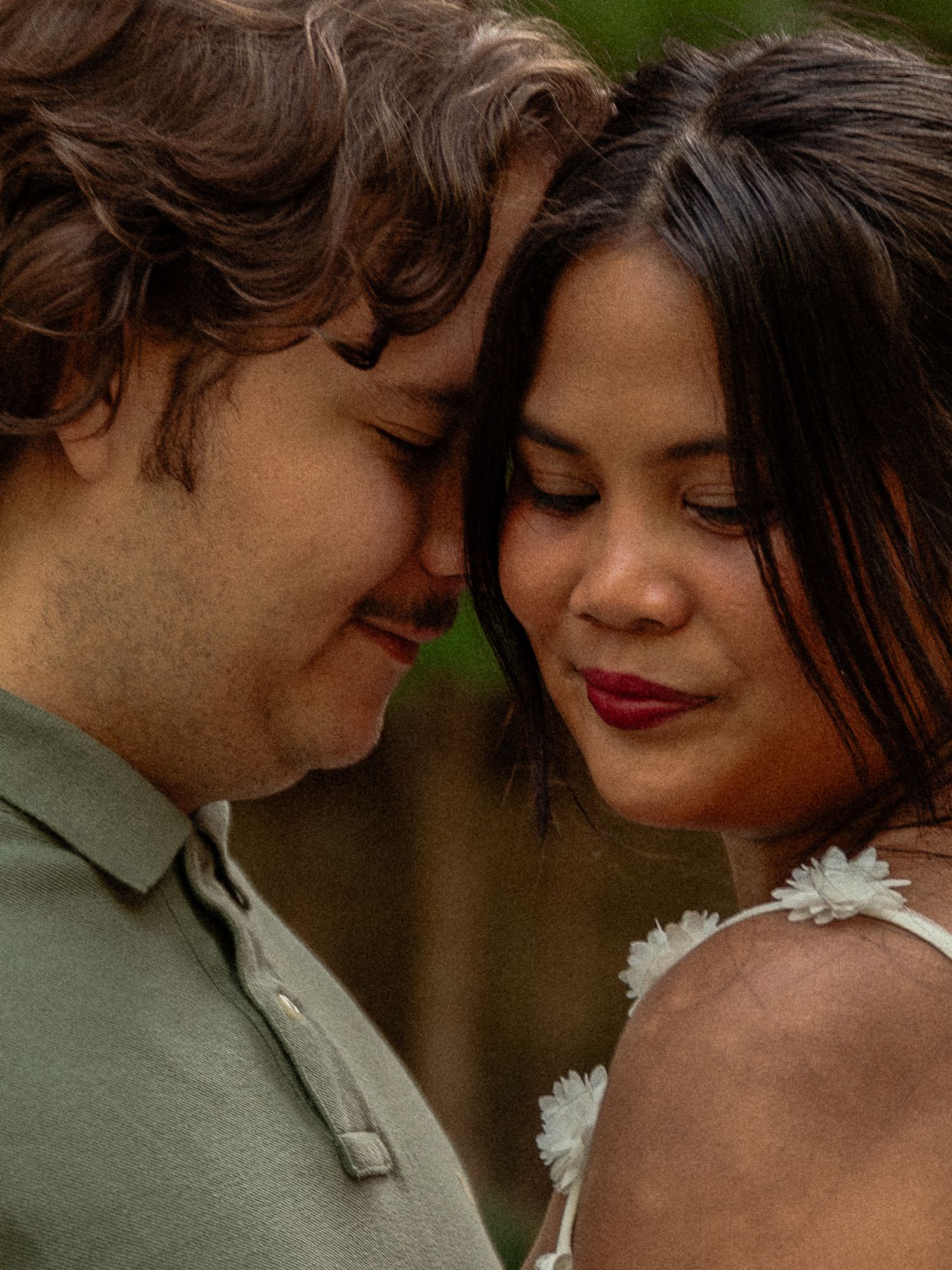 Couple sharing an intimate forehead-to-forehead moment outdoors, woman in floral dress smiling softly.
