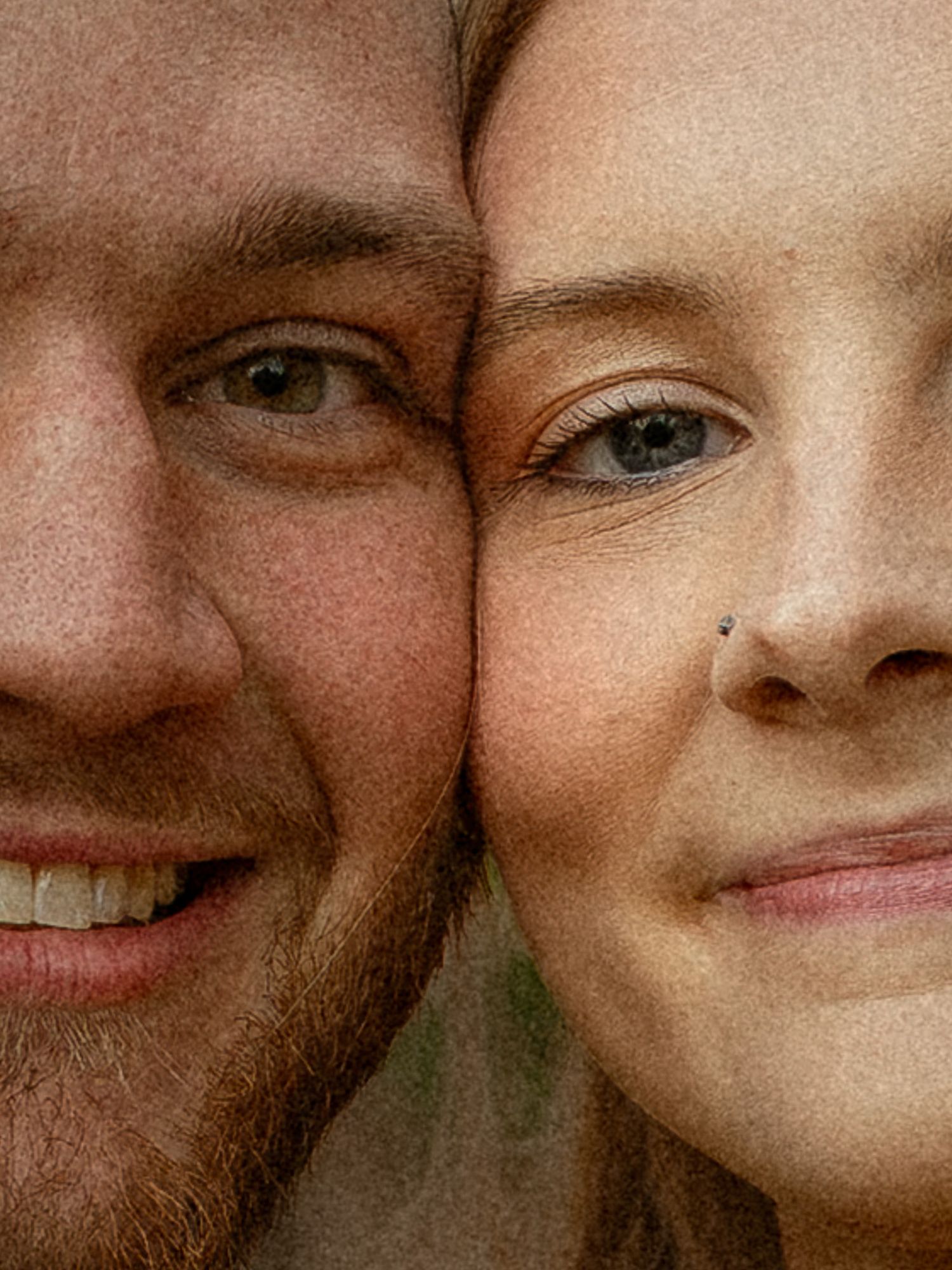 Close-up portrait of a smiling couple with cheeks touching, man with stubble and woman with nose piercing.