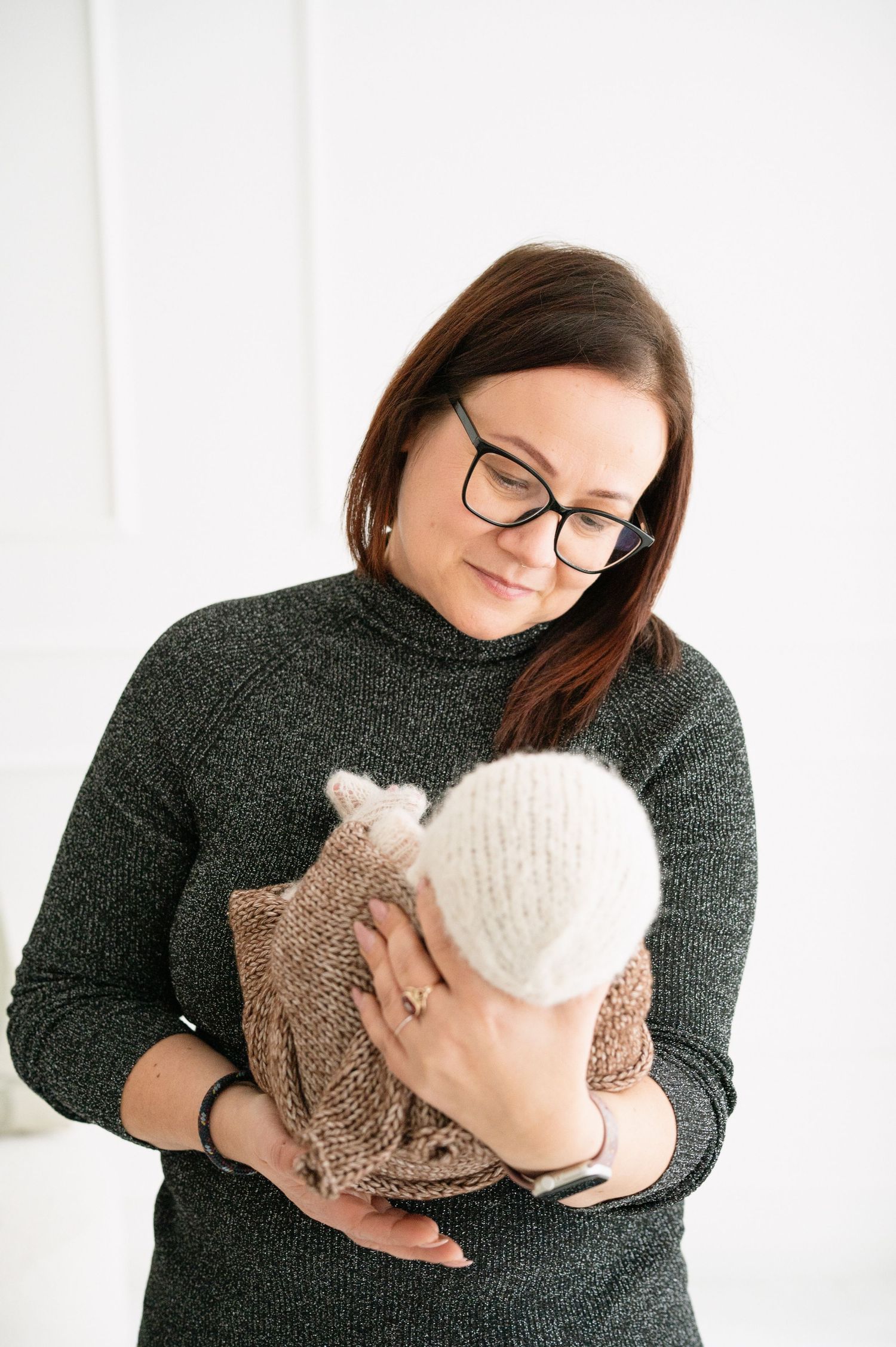 Person wearing glasses and dark sweater holding plush toys in studio setting.