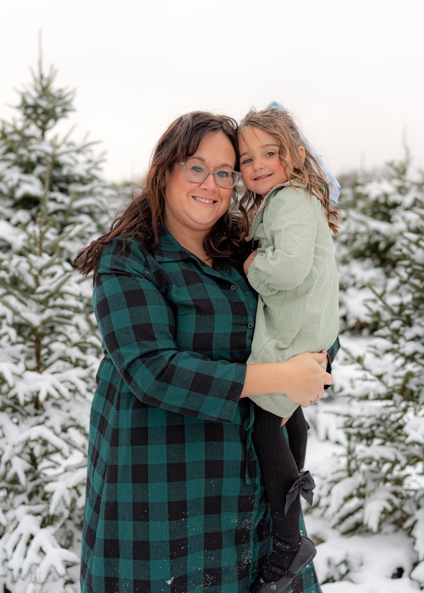 A heartwarming winter photoshoot in a snowy evergreen forest with people embracing and sharing joyful moments together.