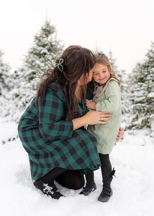 Candid winter photography session with people sharing embraces in the snow surrounded by evergreen trees.
