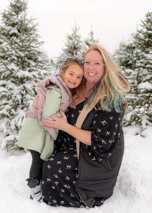 Winter photoshoot featuring people in casual wear playing and laughing in deep snow among pine trees.