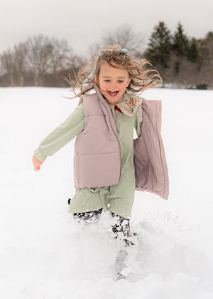 Child playing and jumping through deep snow wearing light colored winter clothing.