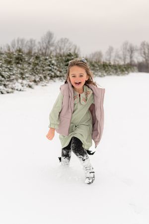 A playful scene in the snow with someone wearing a pink vest and mint green top against a white winter backdrop.
