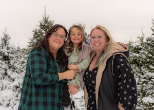 Three people laughing and embracing outdoors in winter with snow-covered trees in the background.