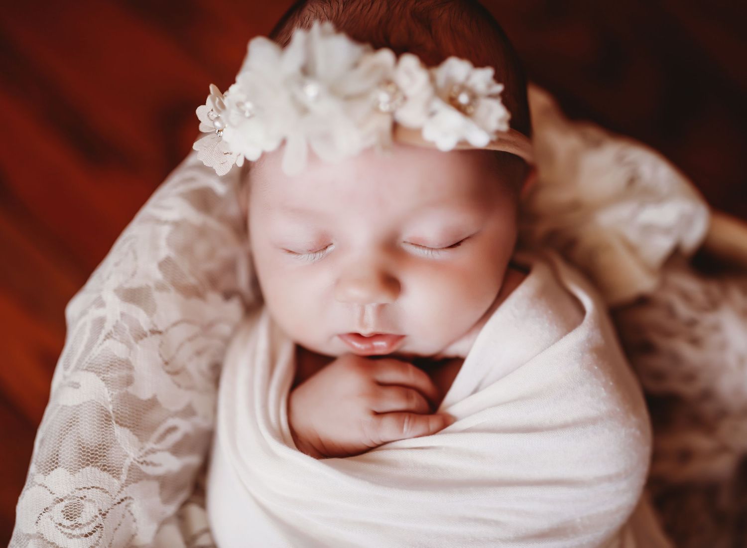 A newborn baby wrapped in white swaddling cloth sleeps peacefully in a series of connected photos.