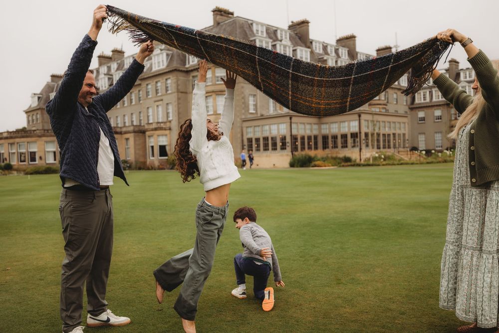Playful outdoor group photo session on a lawn with historic buildings in the background.