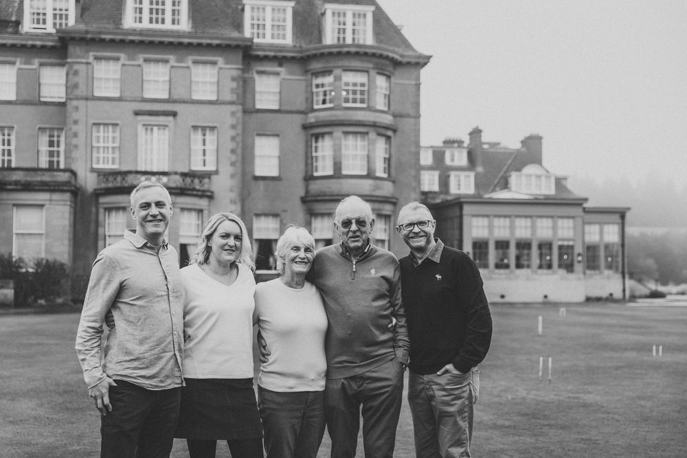 Multiple generations of a family posing for photos in front of a stately brick building.