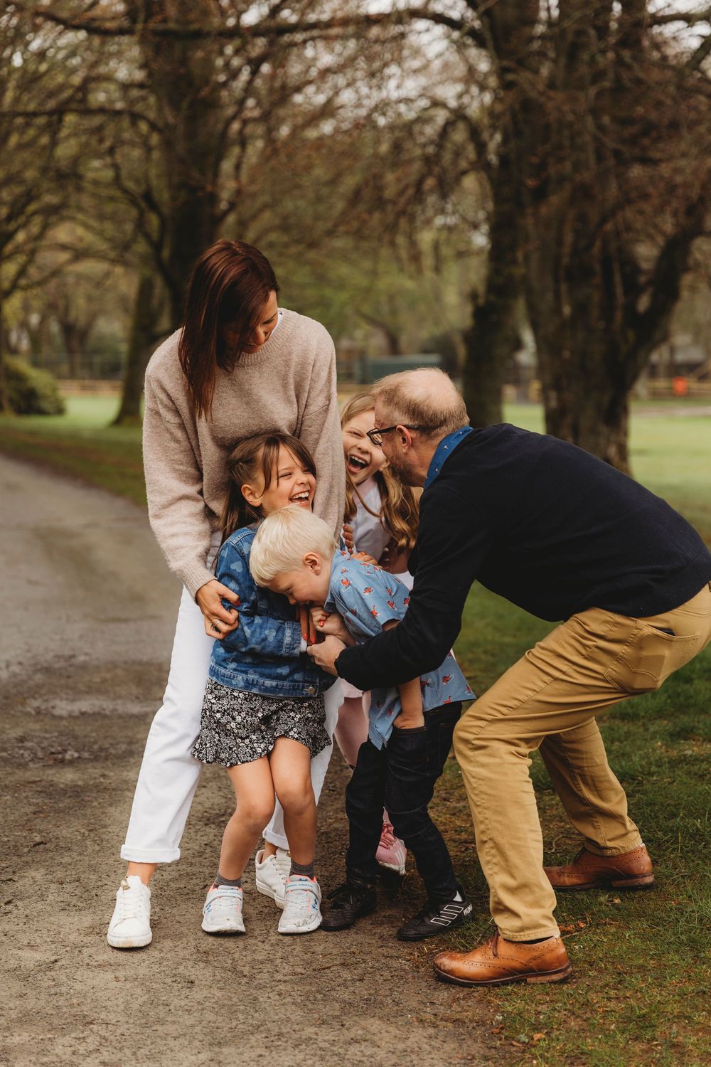 A candid family moment on a tree-lined path in autumn as they share laughter and hugs together.