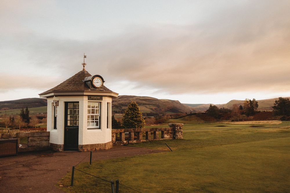A small white gazebo with a clock tower stands on a hilltop overlooking rolling countryside at sunset.
