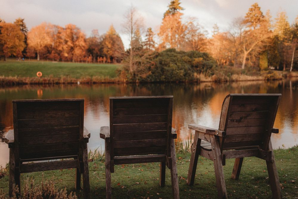 Rustic wooden benches overlook a serene pond at sunset with autumn trees reflecting in the calm water.