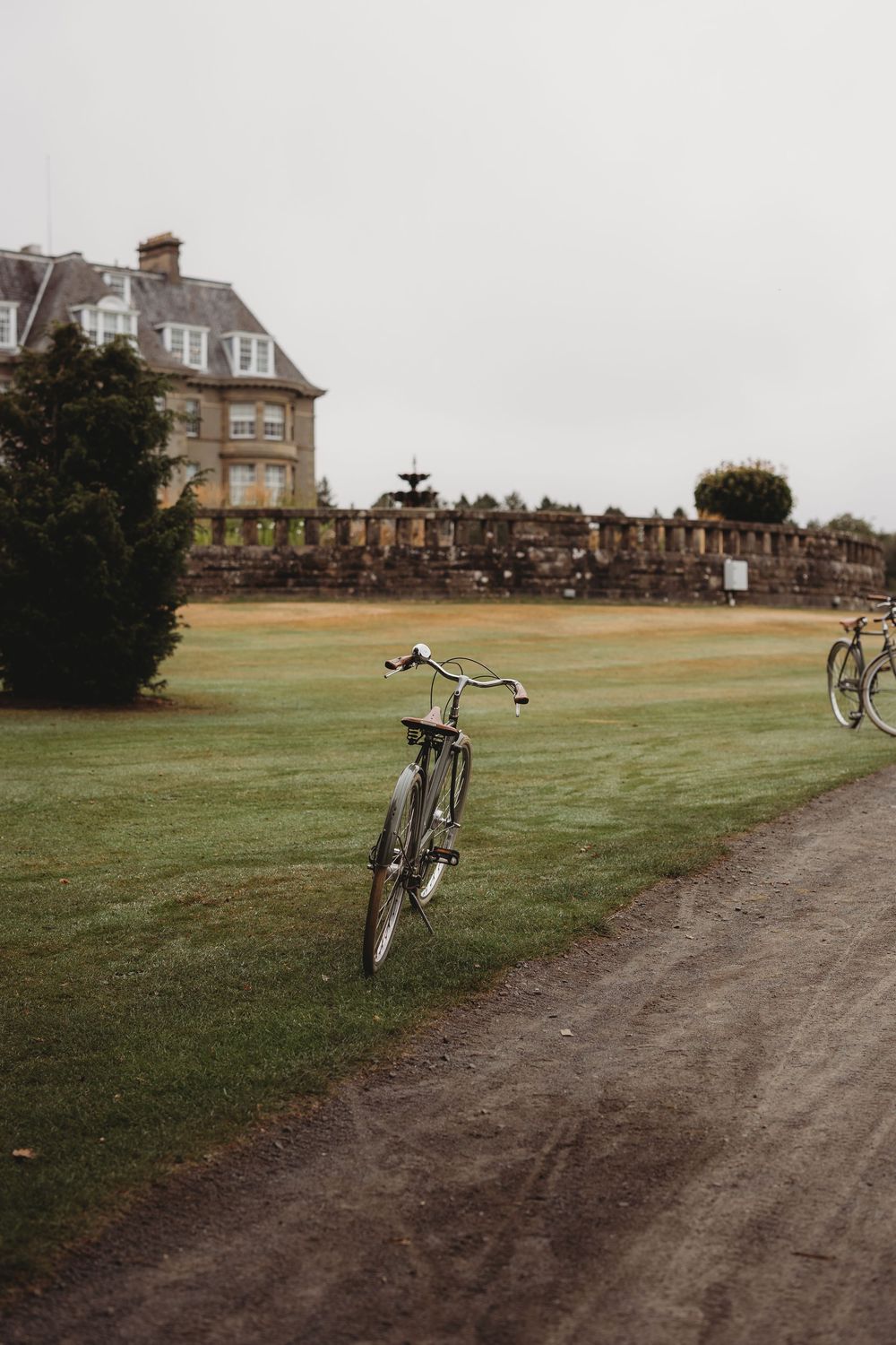 A row of bicycles parked along a dirt path with historic buildings visible in the background on a cloudy day.