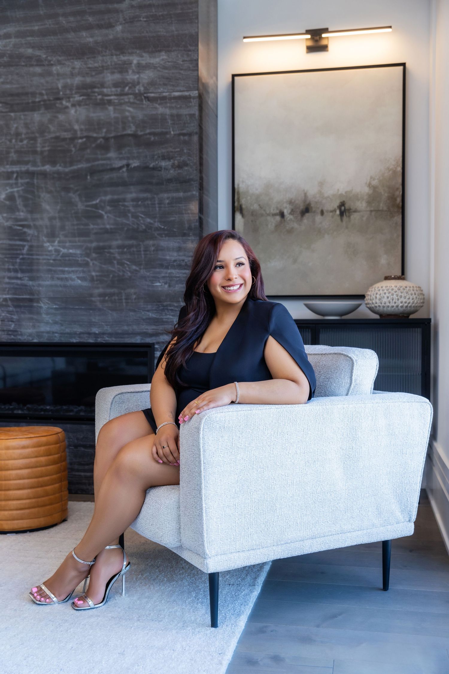 A person in a navy blue blazer and jeans relaxes on a tan leather couch in a bright living room setting.