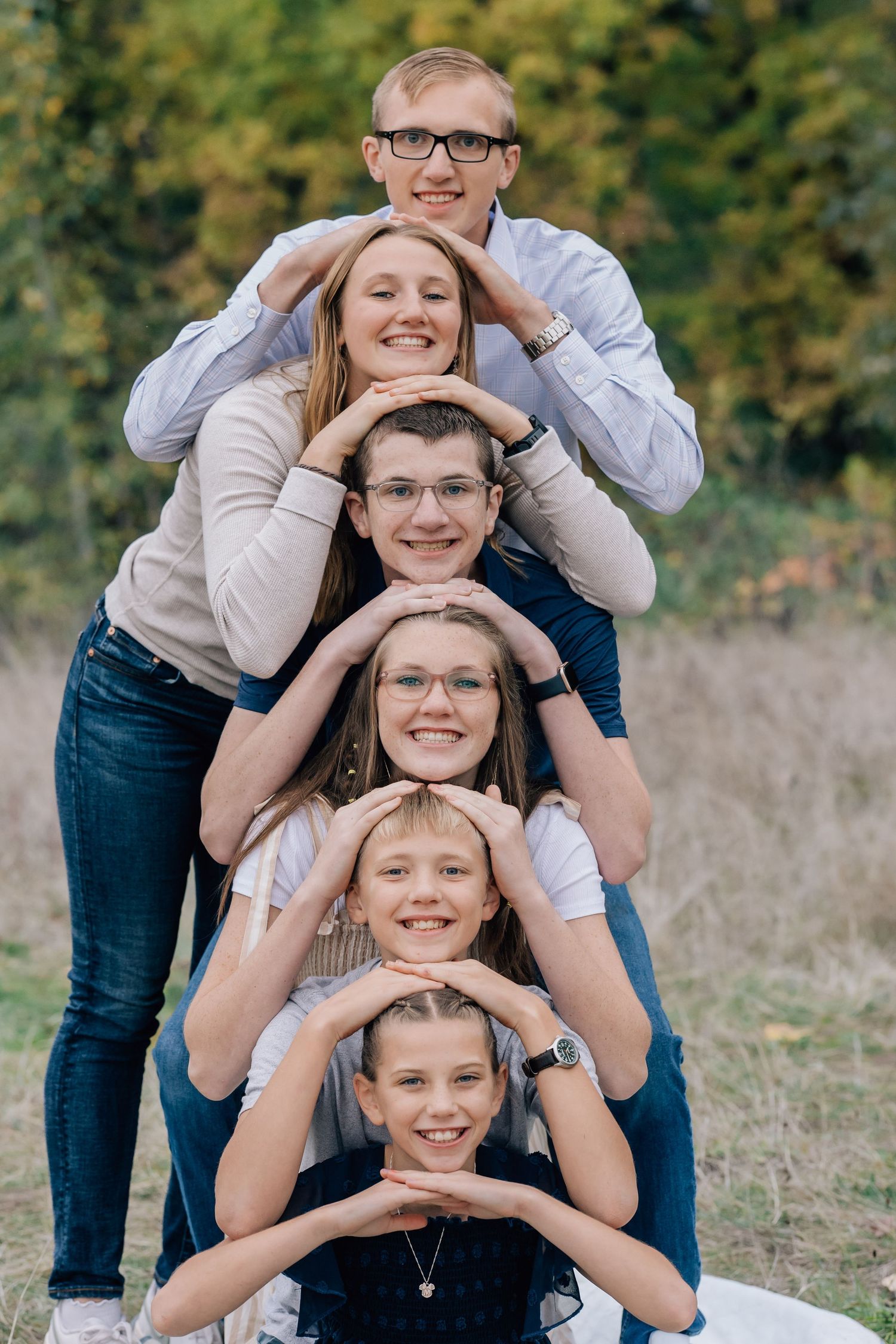 Six siblings posing in a fun stacked totem pole formation outdoors in a green park.