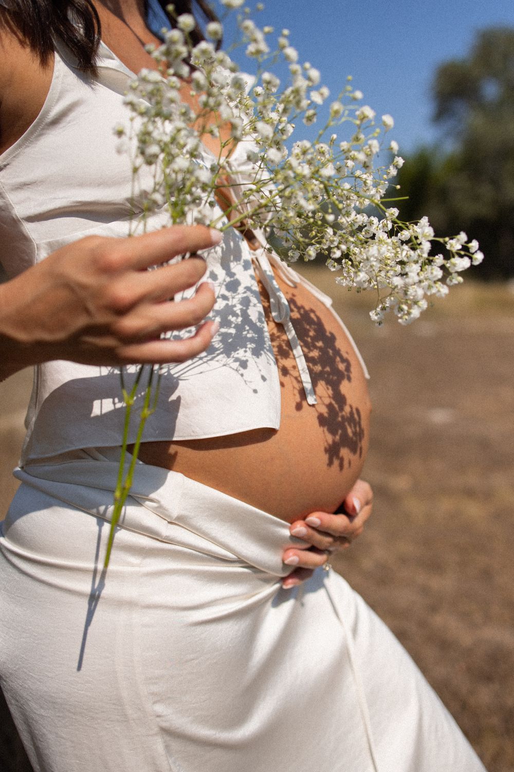 Maternity photos with delicate white flowers against pregnant belly.
