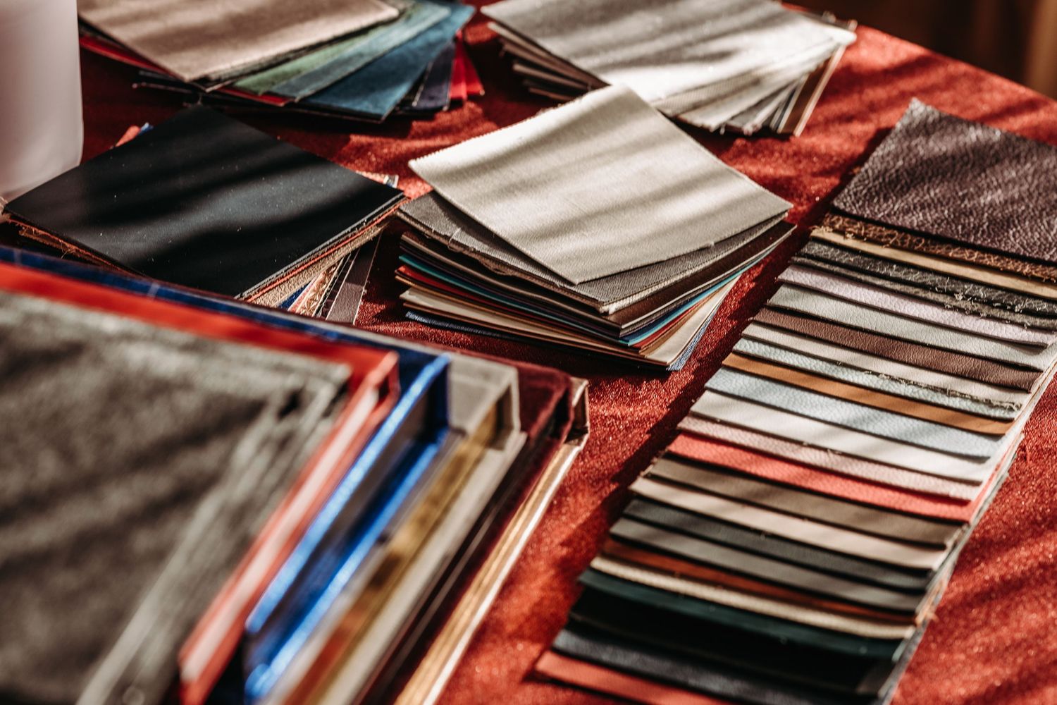 A collection of vinyl records arranged in rows on a red fabric surface showing their sleeves and covers.