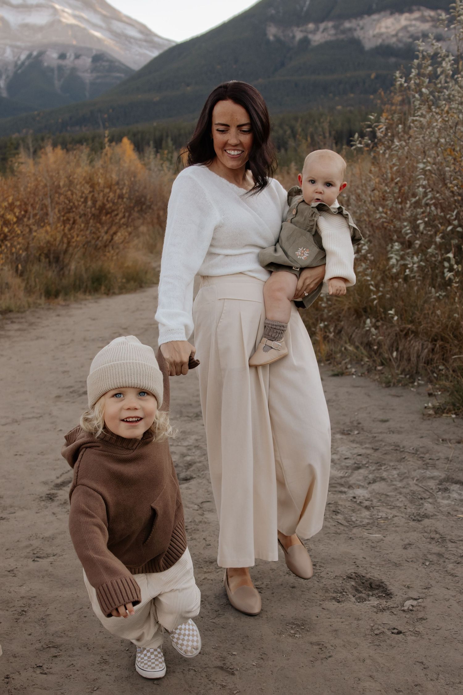 Family in neutral tones playing together against mountain backdrop during autumn.