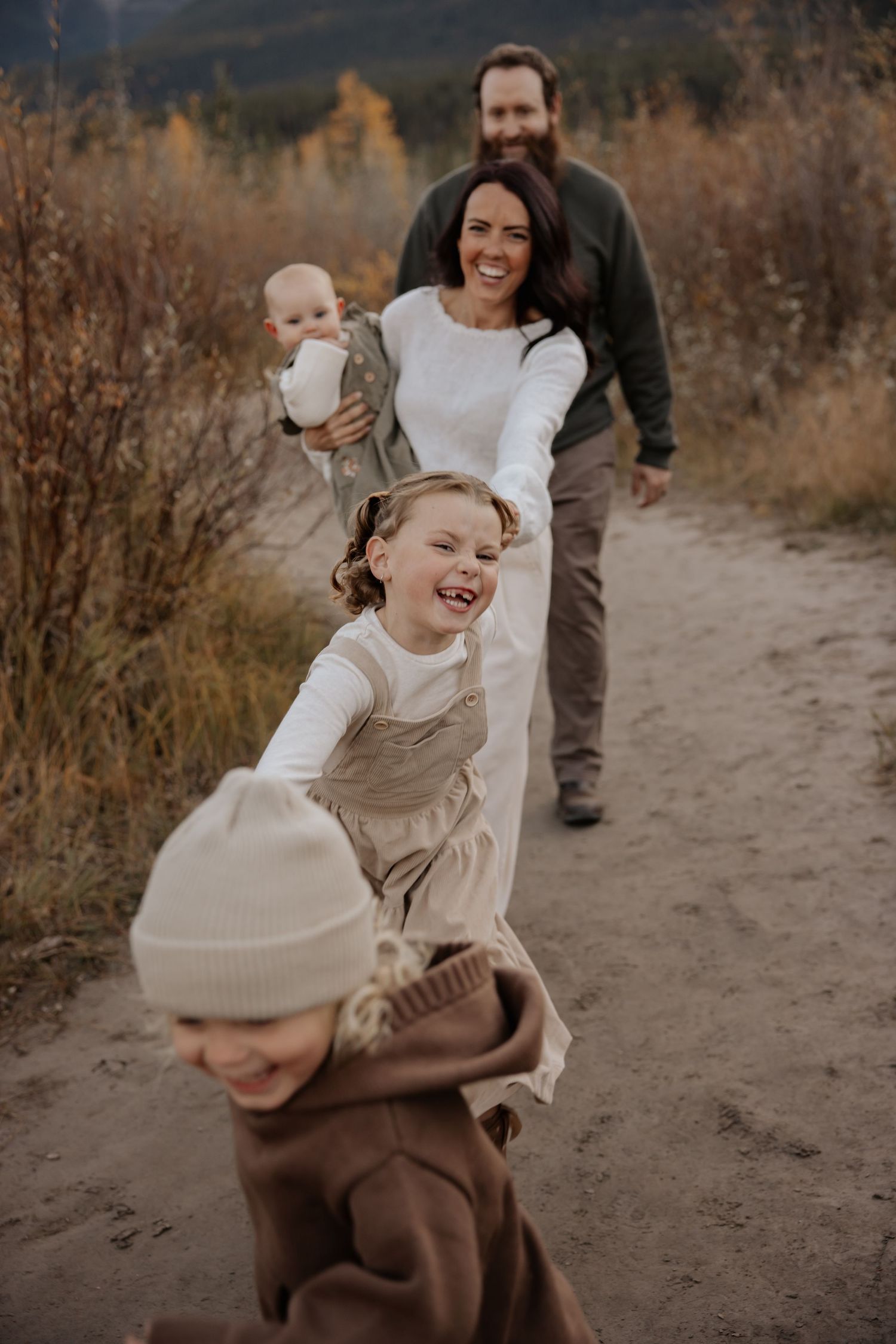 Candid family interactions on dirt path with mountains and autumn foliage in background.