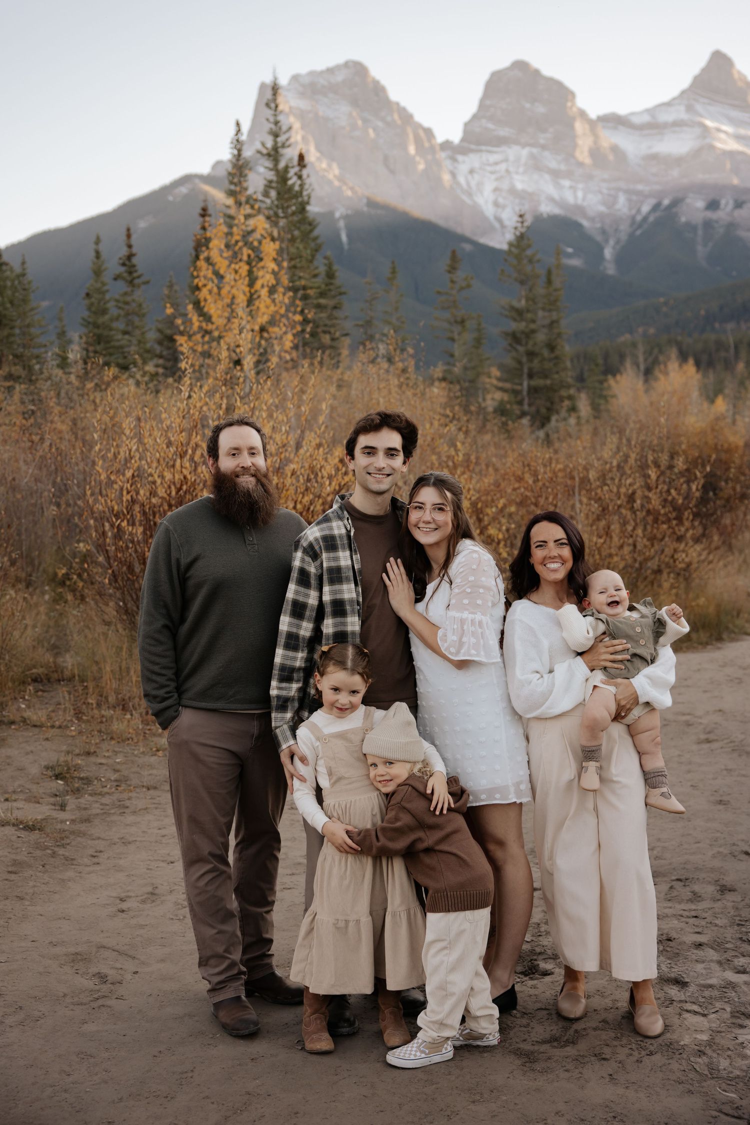 Family portrait in coordinated neutral outfits against mountain backdrop during fall season.