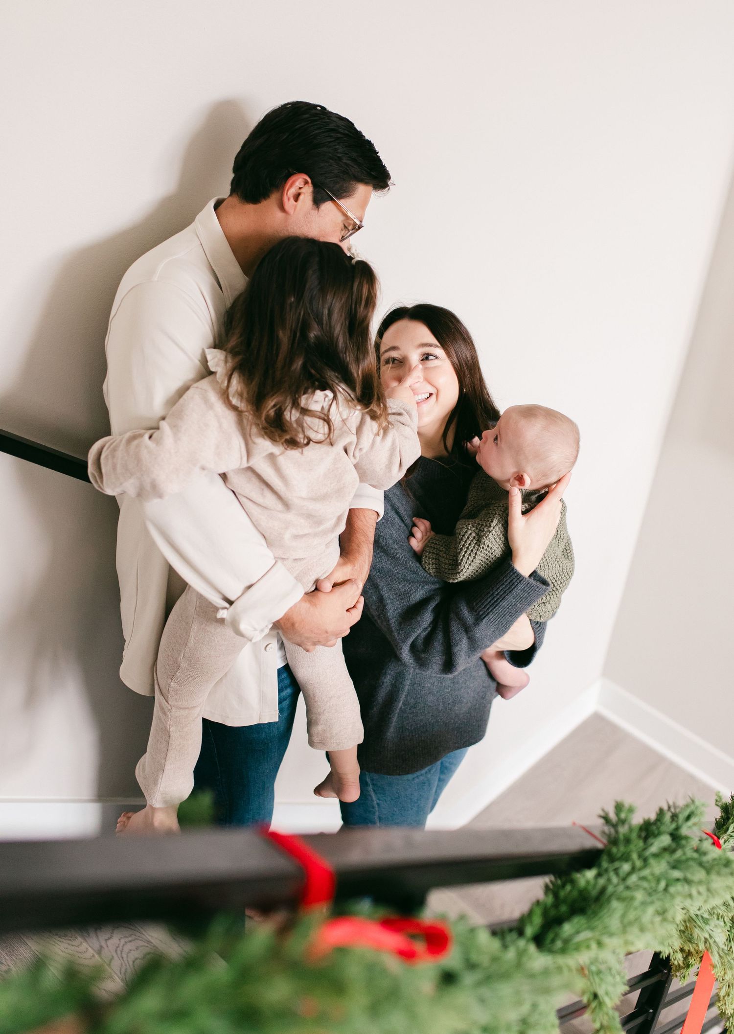 A family shares tender moments together in a series of candid indoor portraits against a white wall.