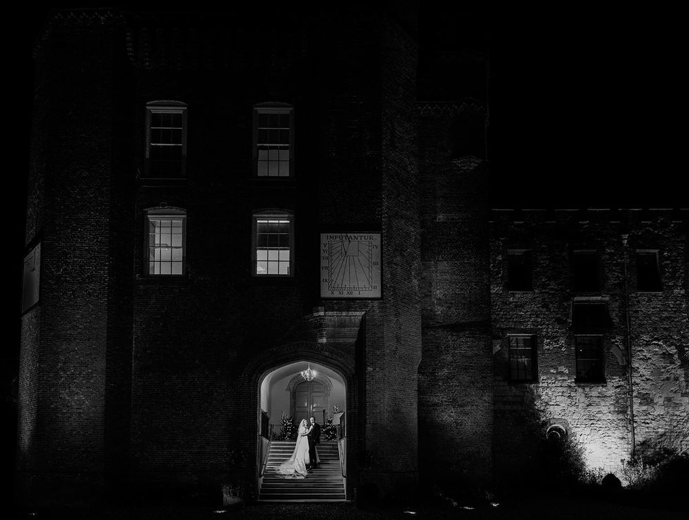 A silhouetted figure stands in an illuminated archway of a dark brick building at night.