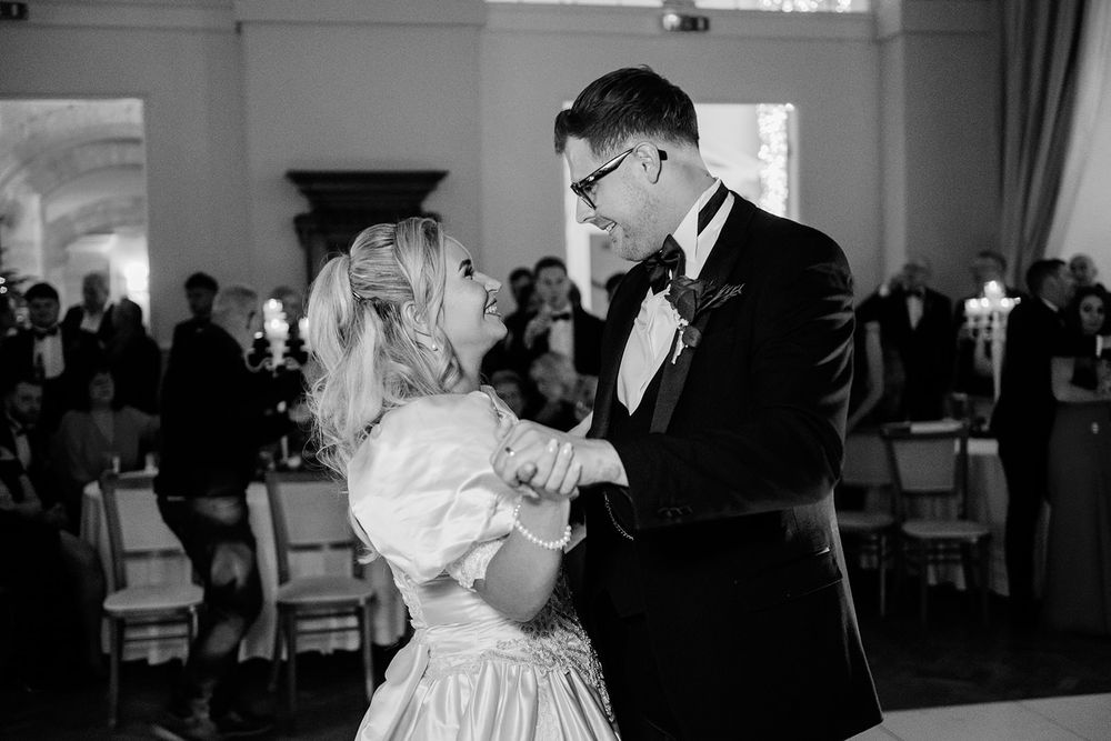 A couple in black and white share an intimate moment during their wedding reception by the cake table.