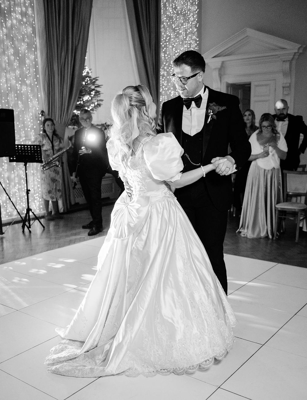 A couple shares a romantic first dance at their wedding reception on an elegant white dance floor with sparkling lights.