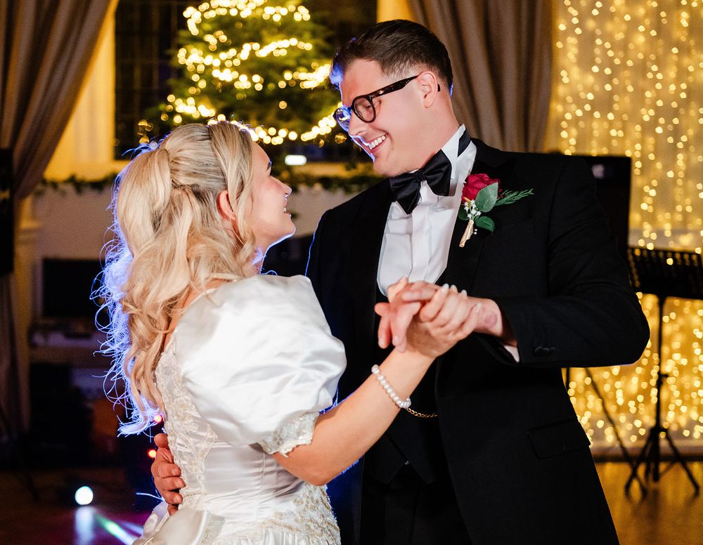 A couple shares a romantic dance at their wedding reception with twinkling lights and decorations in the background.