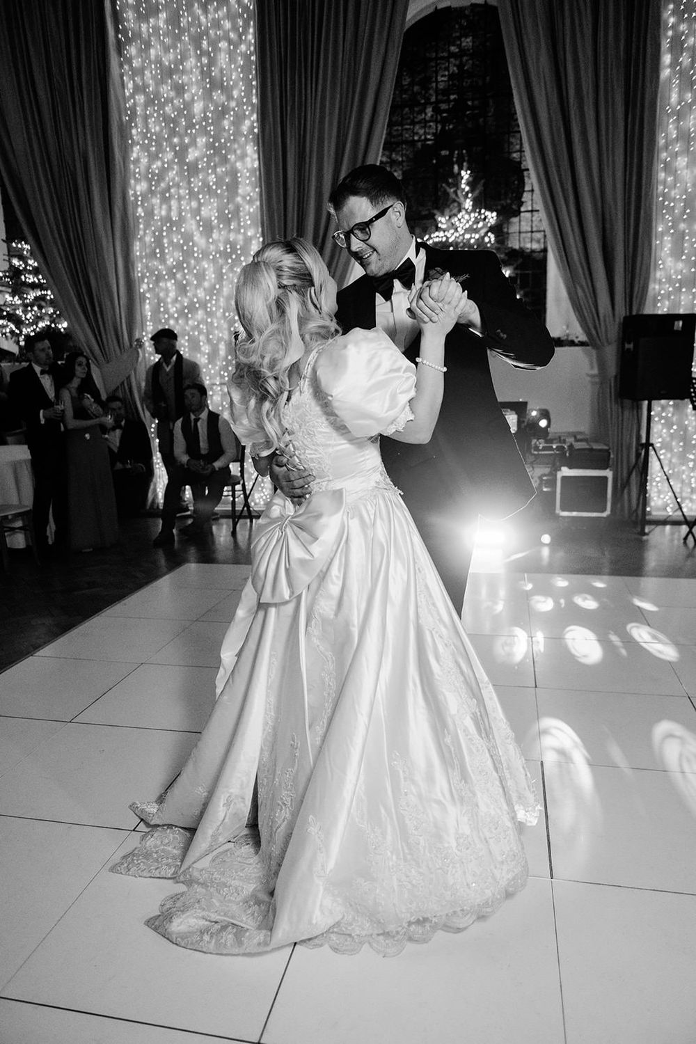 A couple in formal wedding attire shares a romantic dance together on an elegant white dance floor at their reception.