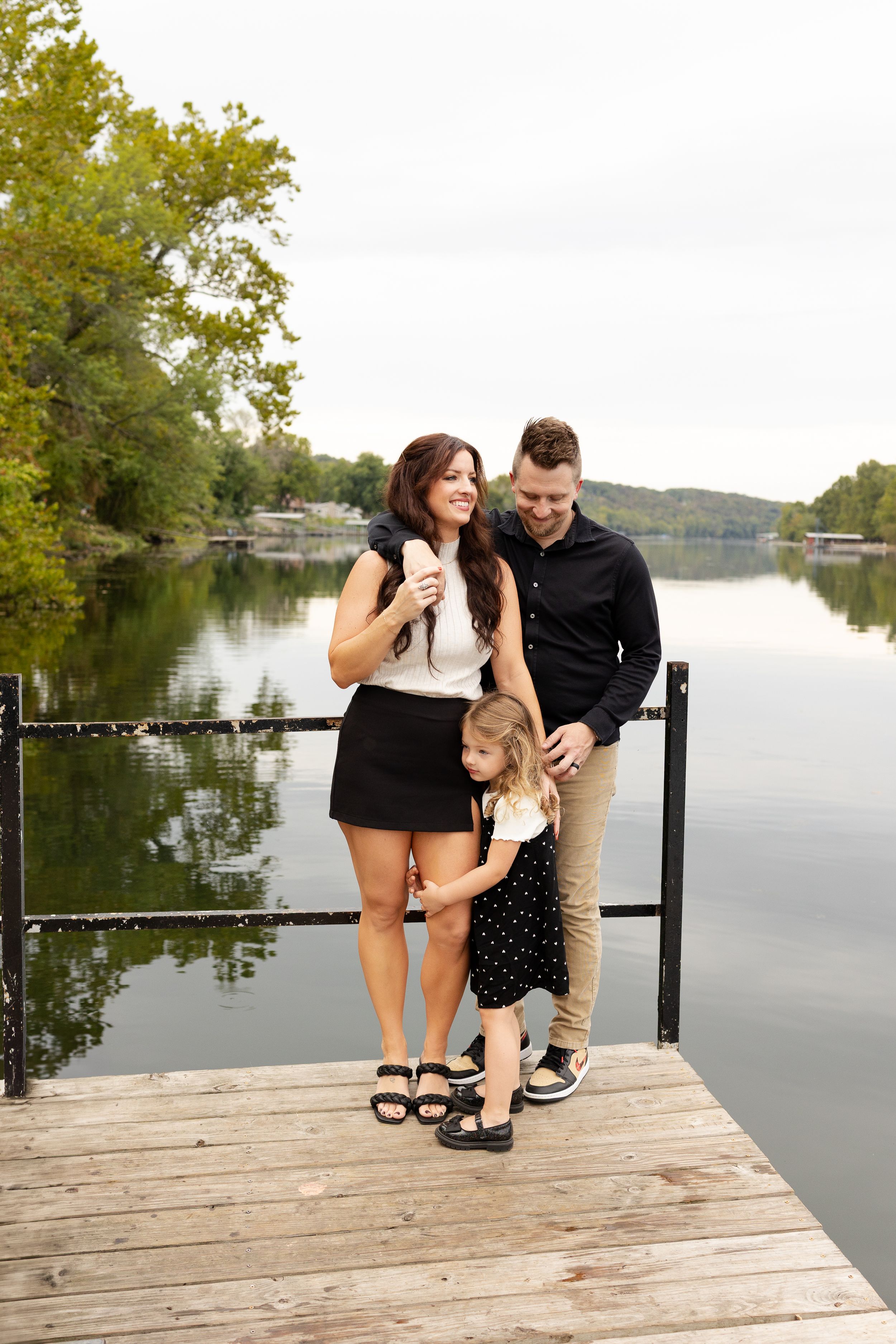 Family enjoying a peaceful moment together on a wooden dock by a serene lake on a sunny autumn day.