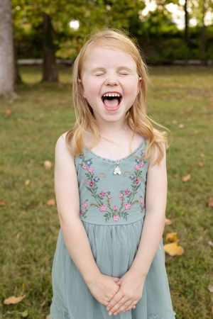 A child in a blue floral dress laughs joyfully while playing outdoors on a sunny autumn day.