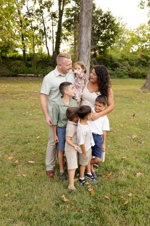A family shares a tender moment together while posing outdoors on a grassy lawn with trees in the background.