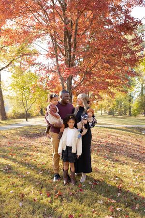 A group enjoys a sunny autumn day outdoors among vibrant red maple trees and fallen leaves on a grassy hillside.