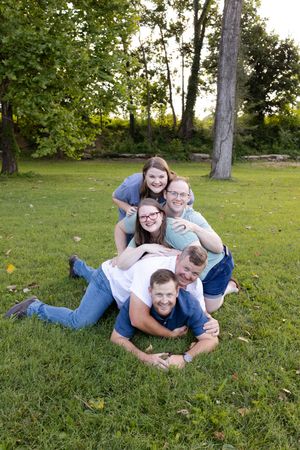 A family lying together playfully on green grass during an outdoor photo session in a park setting.
