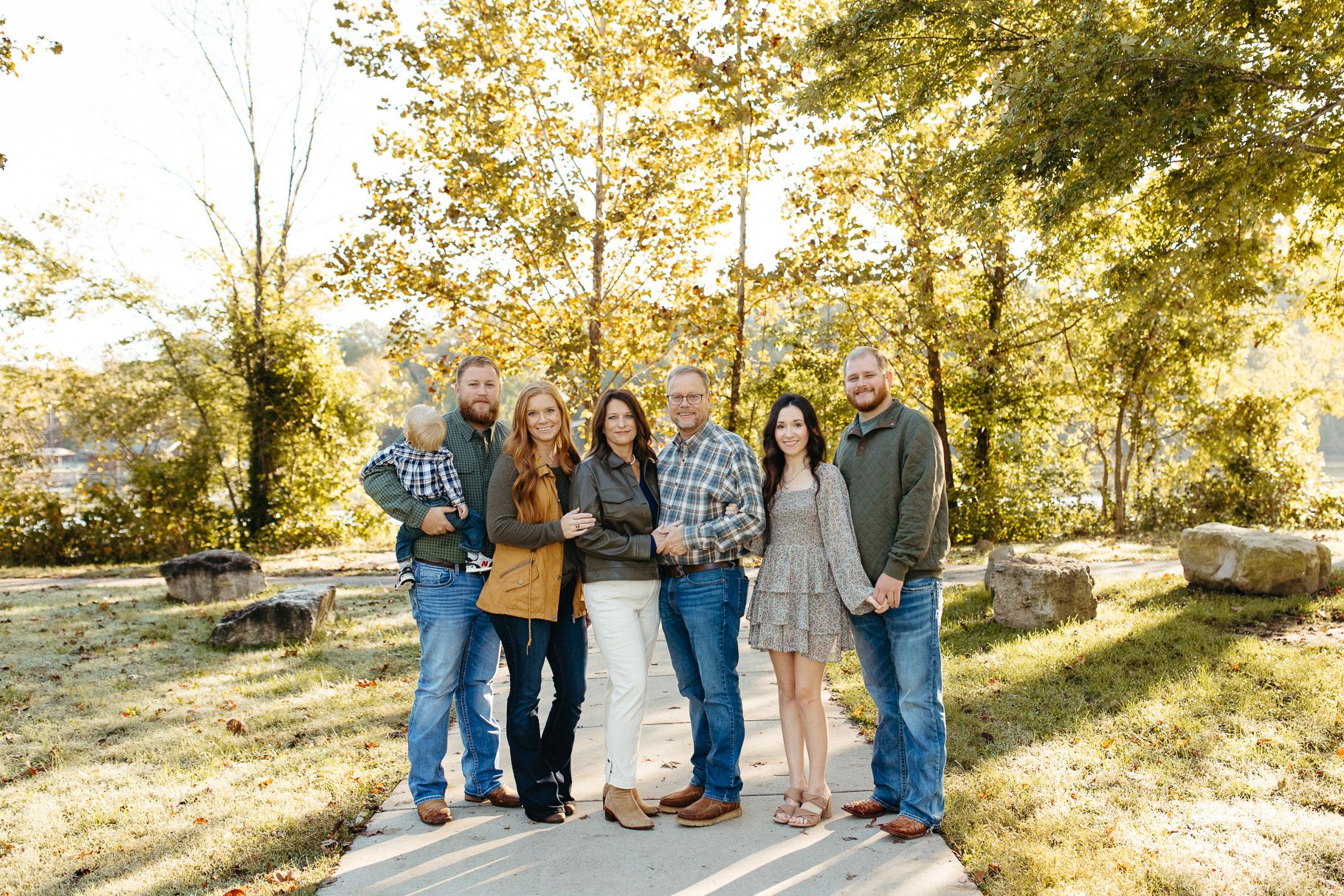A group of people stand together outdoors on a sunny autumn day with golden trees and natural light in the background.