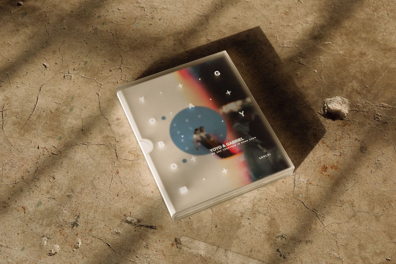 A CD case with abstract artwork featuring a blue circle and white dots lies on a textured concrete surface.