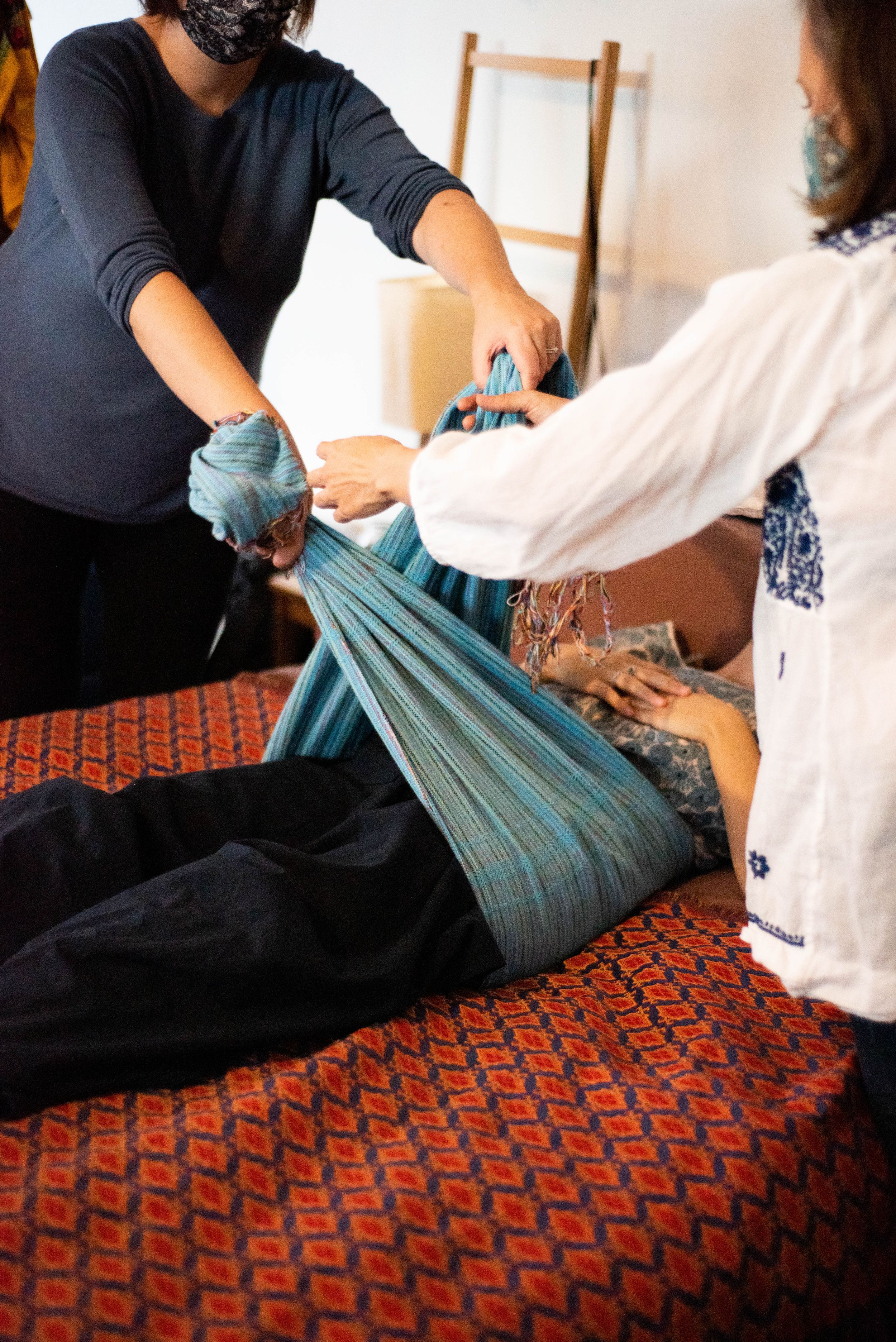 Hands performing traditional Thai massage techniques on a person lying on a patterned red cushion surface.