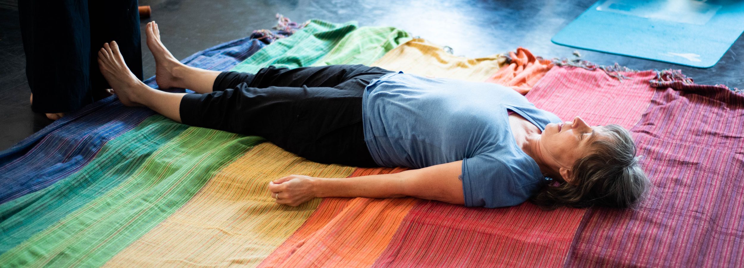 A person lies on a colorful rainbow painted floor while birds fly overhead in a surreal artistic photograph.