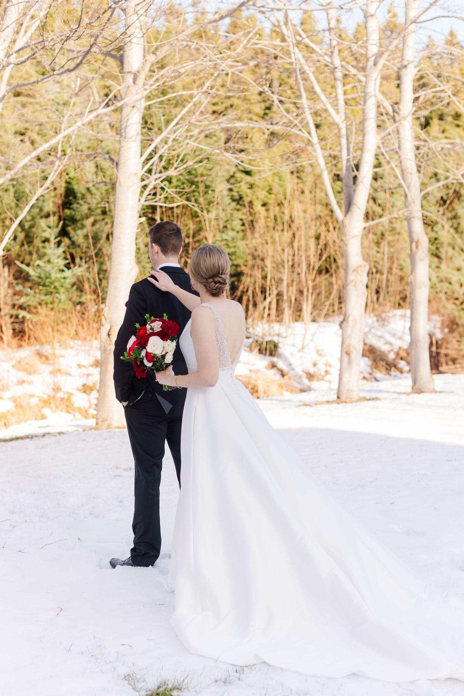 A winter wedding first look moment captured in a snowy forest setting with birch trees.