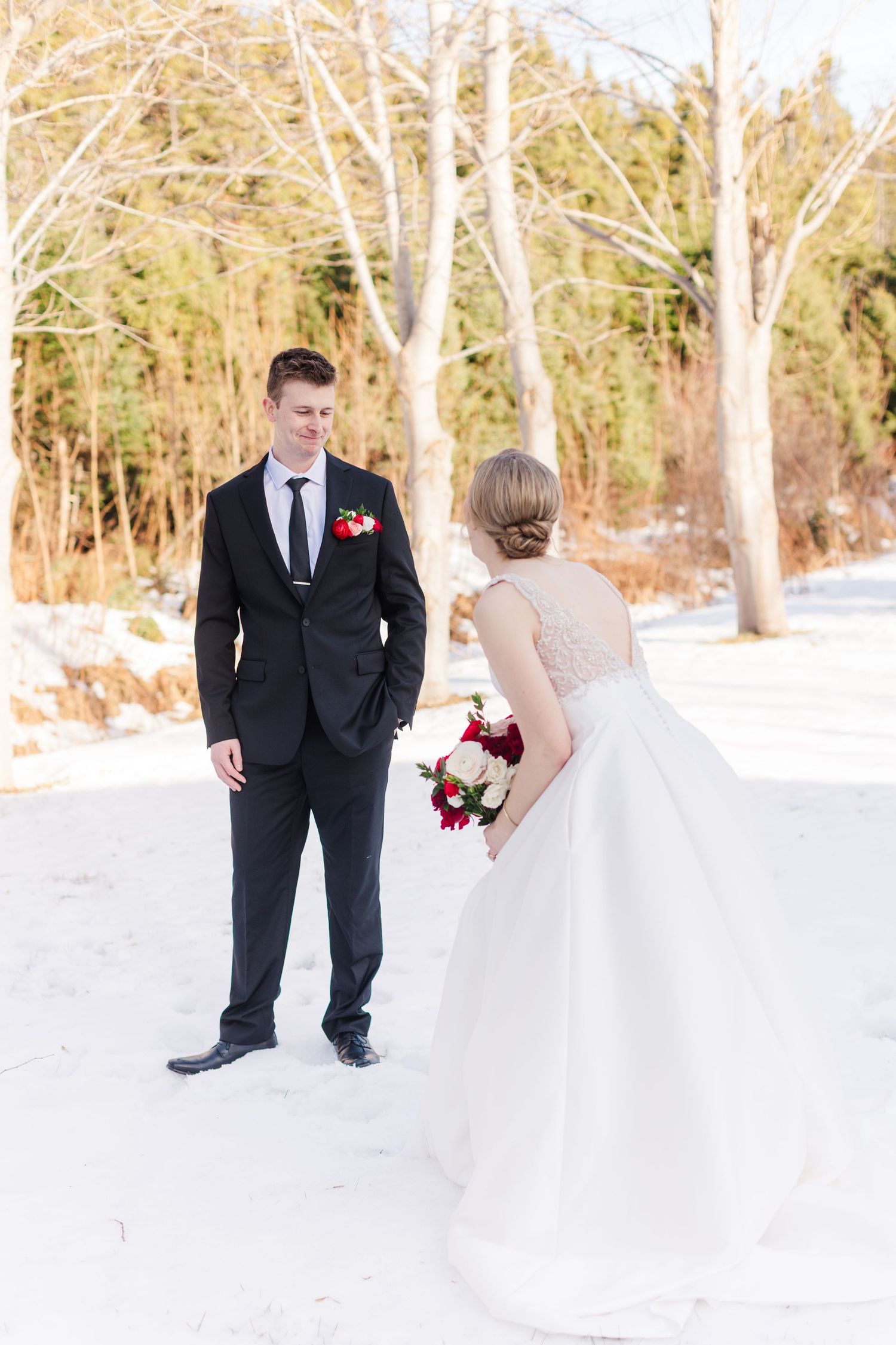A bride and groom share romantic moments in a snowy winter landscape with trees in the background.