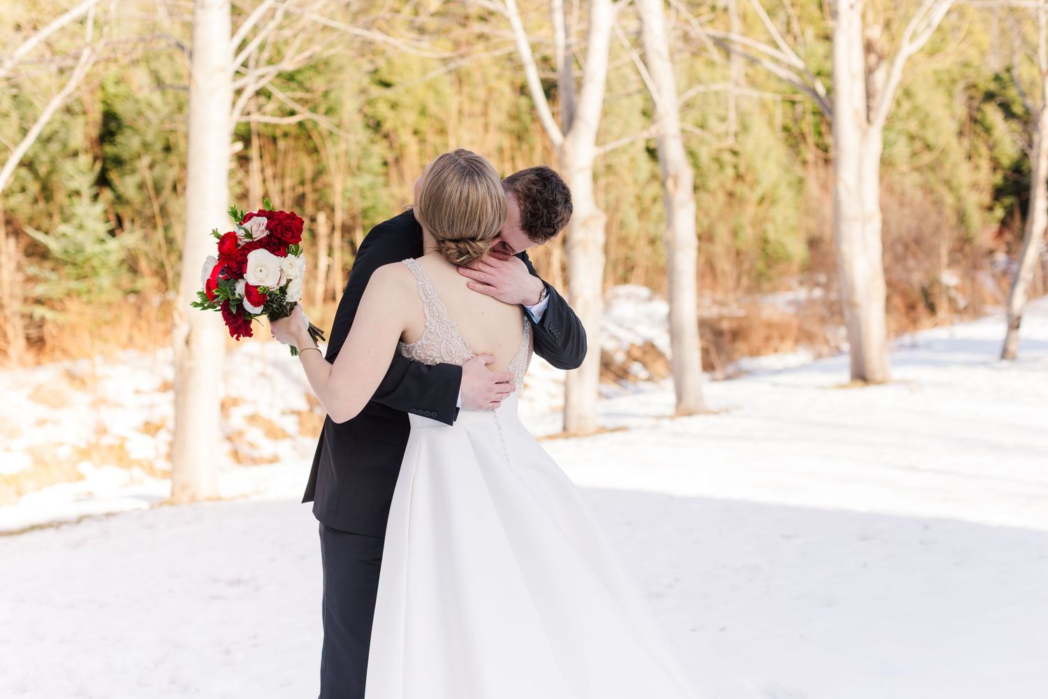 Wedding couple embraces during their winter photo session surrounded by snow and bare trees.