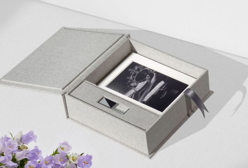An elegant silver photo box with a bow and purple flowers features a black and white photograph displayed inside.