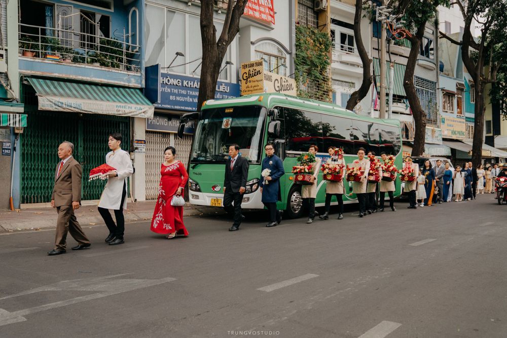 Traditional Vietnamese wedding procession walks along busy urban street beside a green bus.