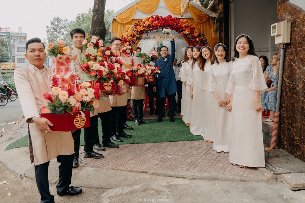 Groom's party with floral bouquets greeted by bridesmaids in white ao dai at Vietnamese wedding.