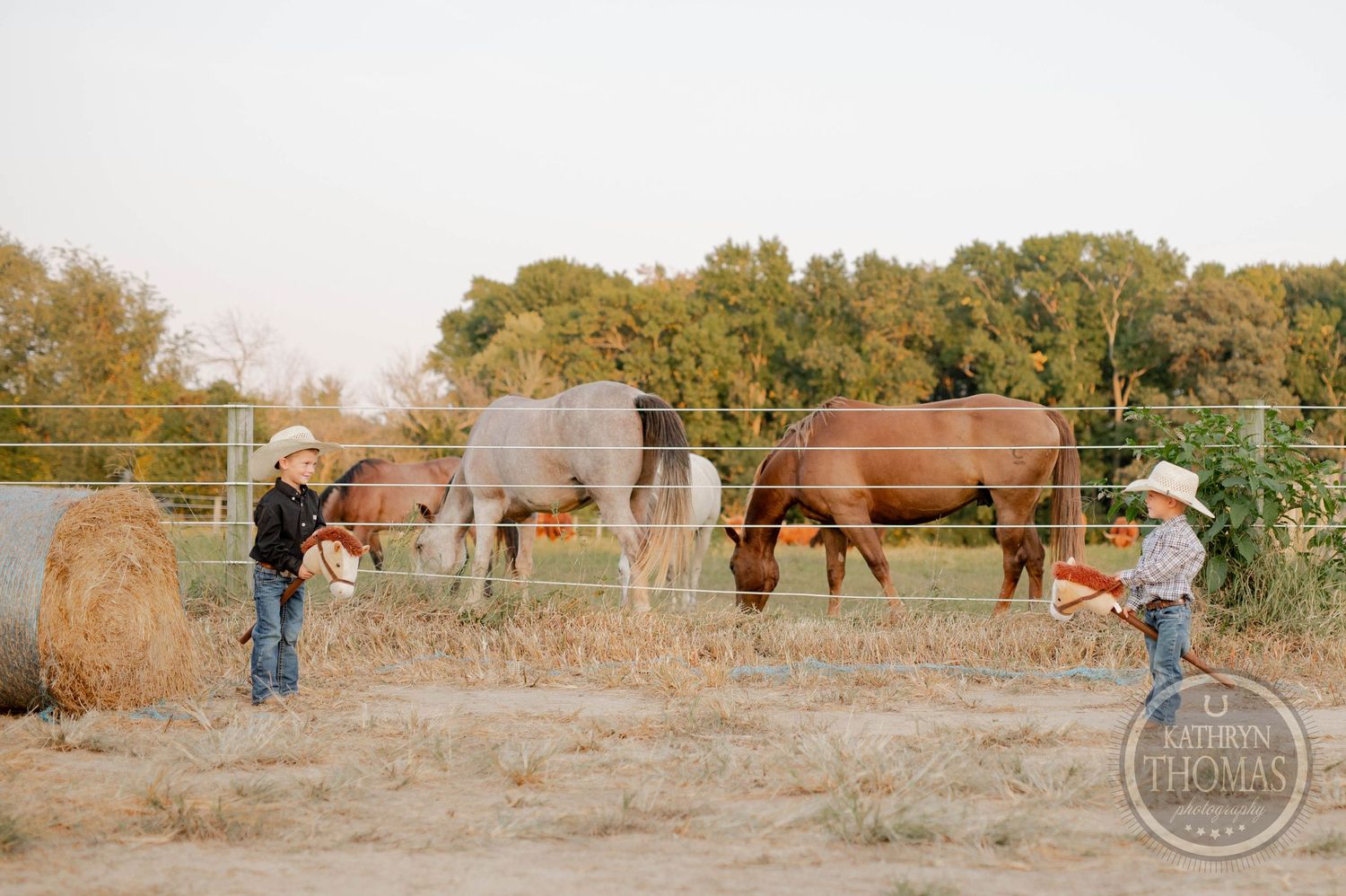 Children in western wear stand near horses grazing in pasture at sunset.