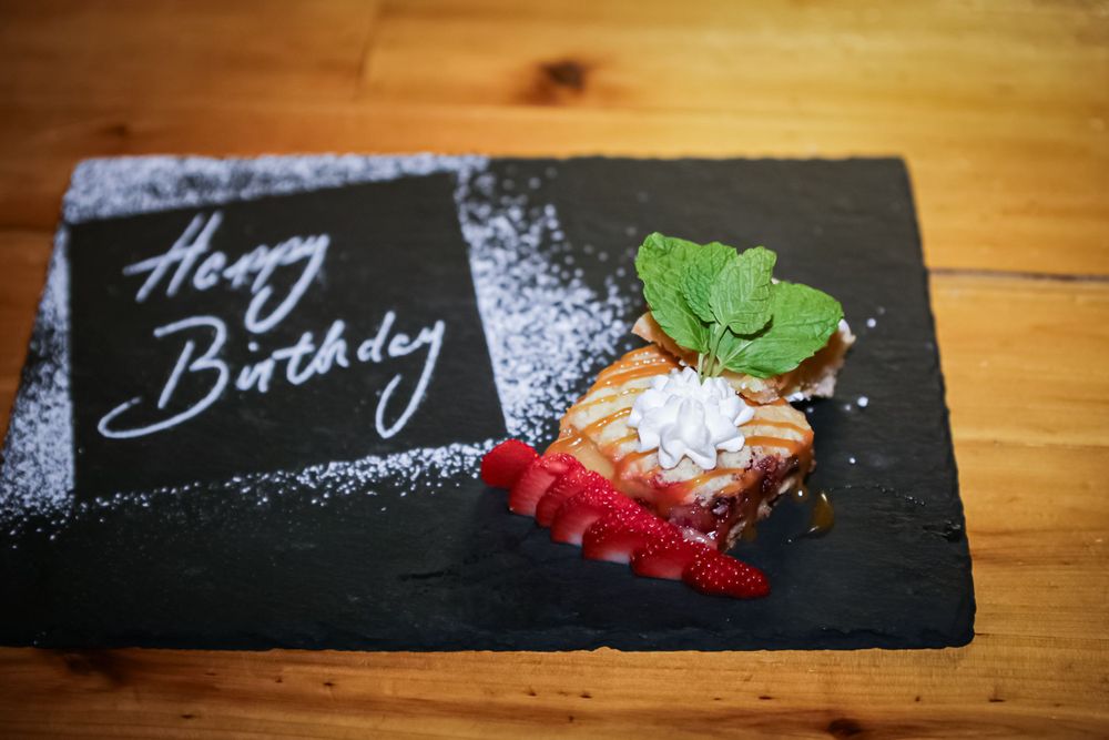 Birthday dessert plates with elegant writing and garnishes on dark slate.