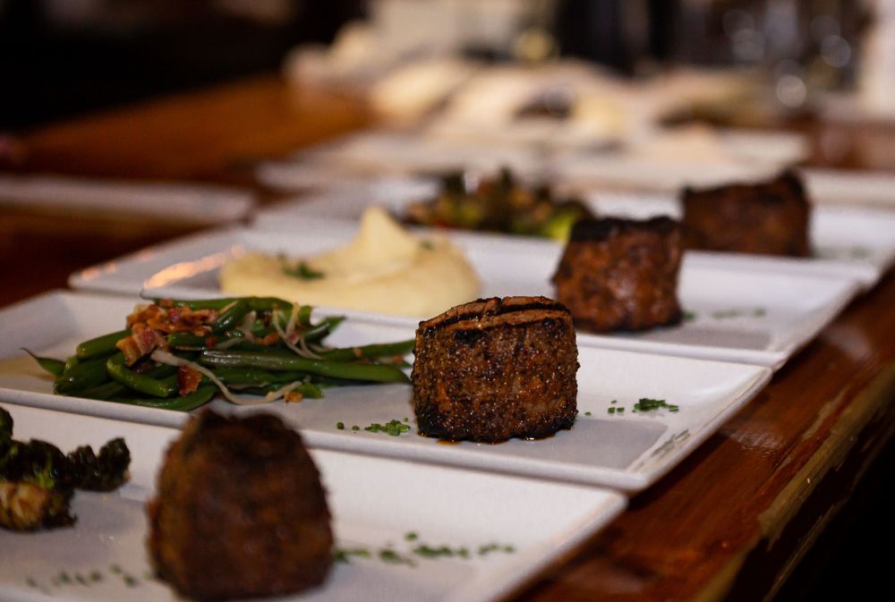 Multiple plates of grilled steaks with sides arranged on a wooden dining table.