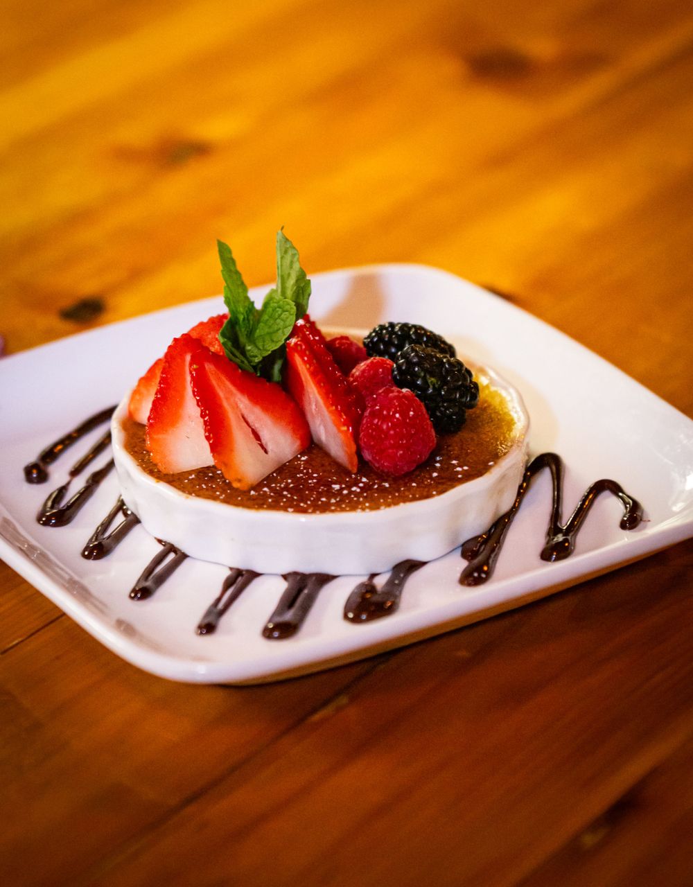 Dessert plates decorated with chocolate sauce and fresh strawberries on wooden table.